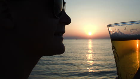 Woman-drinking-beer-on-beach-at-sunset