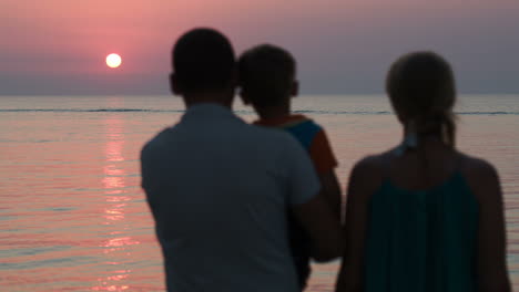 Dreiköpfige-Familie-Beobachtet-Den-Sonnenuntergang-über-Dem-Meer
