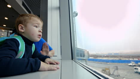 Mother-and-little-son-looking-out-the-window-at-airport