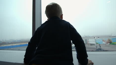 Boy-looking-at-the-plane-from-window-and-imitating-it