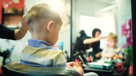 Hairdresser-cutting-childs-hair-while-he-playing-with-a-toy