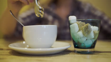 Woman-putting-sugar-into-tea-cup-using-tongs