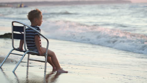 Boy-sitting-on-the-chair-by-sea-waves-washing-his-feet