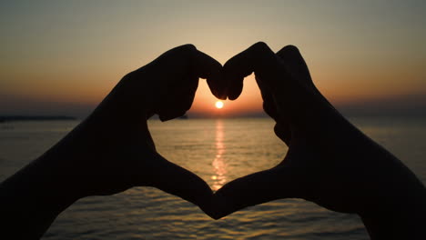 Sunset-over-sea-in-heart-made-of-hands
