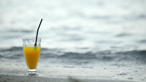 Glass-of-cocktail-on-beach-and-waves-washing-shore