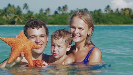 Parents-and-son-in-sea-water-holding-starfish