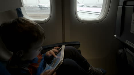 Boy-sitting-in-the-plane-and-using-tablet-PC