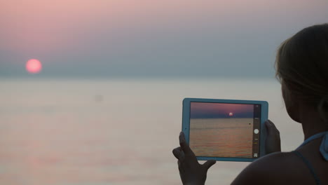 Woman-making-photo-of-sunset-using-tablet-PC