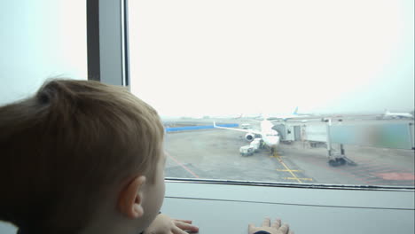 Little-boy-looking-out-window-and-pointing-at-plane
