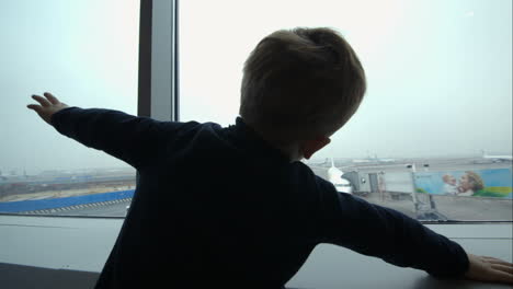 Little-boy-showing-plane-with-hands-looking-at-it-out-the-window