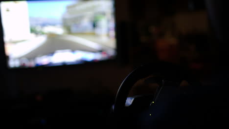 Man-playing-racing-game-with-steering-wheel-in-darkness