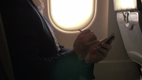 Man-using-pen-to-type-on-smart-phone-in-plane