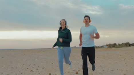 Young-couple-in-headphones-running-on-the-beach