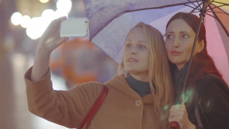 Two-women-friends-making-selfie-with-umbrella-on-rainy-day