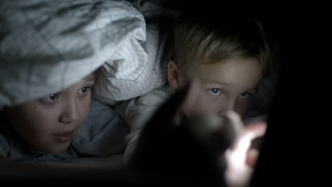 Two-boys-lying-in-bed-at-night-watching-movie-on-pad