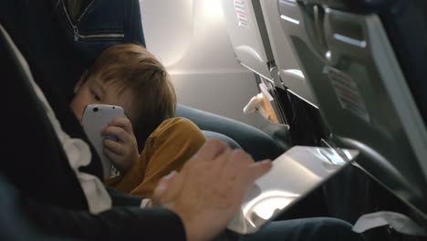Child-with-cell-and-and-man-using-pad-in-plane