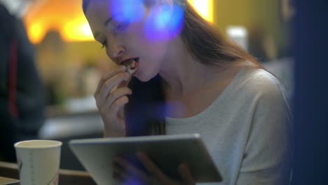 Brunette-woman-eats-cake-while-reading-on-electronic-tablet