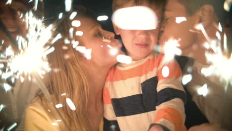 Family-of-three-holding-sparklers-and-kissing