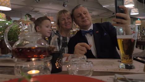 Grandparents-and-grandson-making-selfie-during-family-dinner-in-restaurant