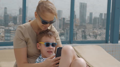 Mutter-Und-Kind-Nutzen-Ihr-Mobiltelefon-Beim-Entspannen-Auf-Dem-Dach-Eines-Hotels-In-Tel-Aviv,-Israel