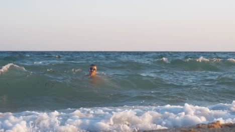 Excited-child-swimming-in-wavy-sea-at-sunset