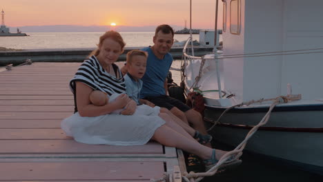 Parents-with-elder-son-and-baby-sitting-on-the-pier-at-sunset