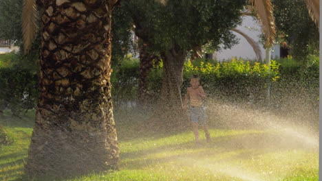 Child-running-on-the-lawn-and-getting-wet-from-water-sprinkler