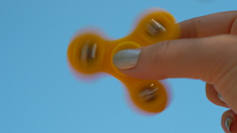 Playing-with-yellow-fidget-spinner-on-sky-background