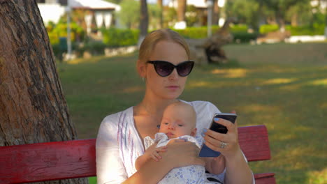 Frau-Benutzt-Handy-Während-Eines-Ausflugs-Mit-Baby-Im-Park