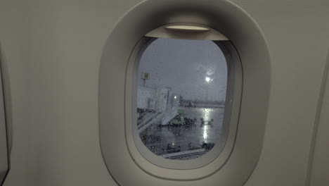 A-closeup-of-a-porthole-and-a-rainy-airport-courtyard-behind-it