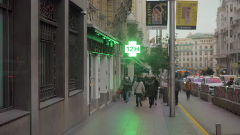 Street-with-walking-people-and-pharmacy-sign-in-Madrid-Spain