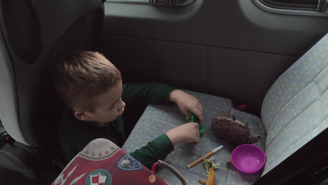 A-boy-sitting-on-a-cars-floor-playing-with-some-toys-on-a-back-seat