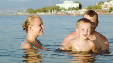 Glückliche-Eltern-Und-Sohn-Baden-Im-Meer-Im-Resort
