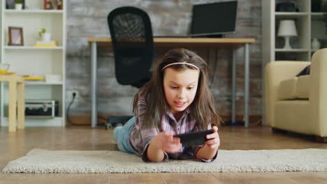 Fröhliches-Kleines-Mädchen,-Das-Auf-Dem-Boden-Liegt-Und-Videospiele-Spielt
