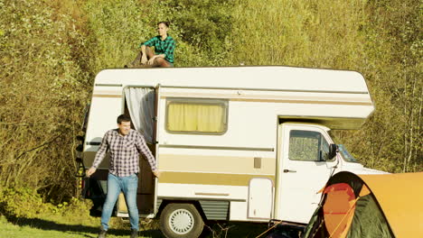 Young-girl-relaxing-on-top-of-retro-camper-van-in-mountain-wilderness
