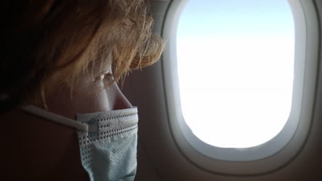 Junge-Mit-Maske-Schaut-Durch-Das-Flugzeugfenster