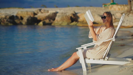 Woman-with-pad-making-photos-of-sea-sitting-in-deck-chair-on-beach
