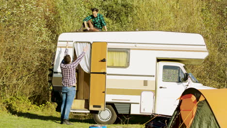Boyfriend-saying-hello-to-her-girlfriend-who's-relaxing-on-top-of-their-vintage-camper-van