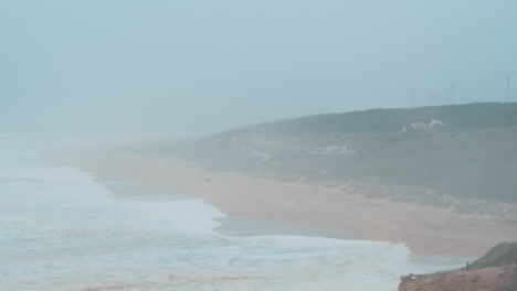 Misty-ocean-coast-with-distant-wind-turbines-in-Nazare-Portugal