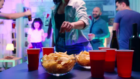 Young-woman-at-a-party-with-neon-light-taking-chips-from-the-table-and-a-cup-of-beer