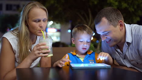 Junge-Sitzt-Mit-Seinen-Eltern-Im-Café-Und-Benutzt-Einen-Tablet-PC