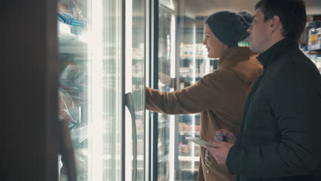 Young-couple-taking-frozen-food-from-fridge-in-the-shop