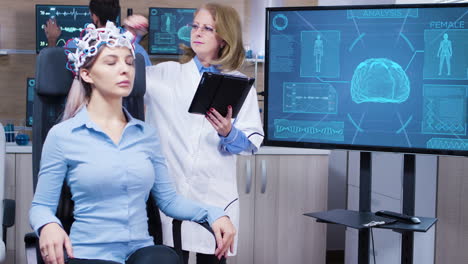 Female-scientis-in-brain-activity-using-her-tablet-to-make-adjustmest-on-her-patient-headset