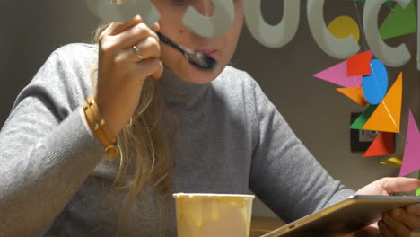 Woman-in-cafe-eating-ice-cream-and-using-pad