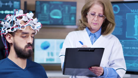 Female-doctor-taking-notes-while-patient-is-wearing-brains-sensors