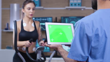 Arzt-Hält-Tablet-Mit-Grünem-Bildschirm-Vor-Sportler