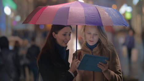 Female-friends-using-touch-pad-on-rainy-evening-in-city
