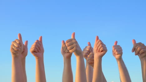 Hands-up-with-thumbs-up-against-blue-sky