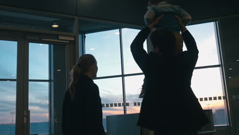 Young-family-looking-out-airport-window-at-sunset