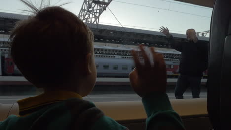 Child-in-train-waving-hand-to-grandparents-as-he-leaving